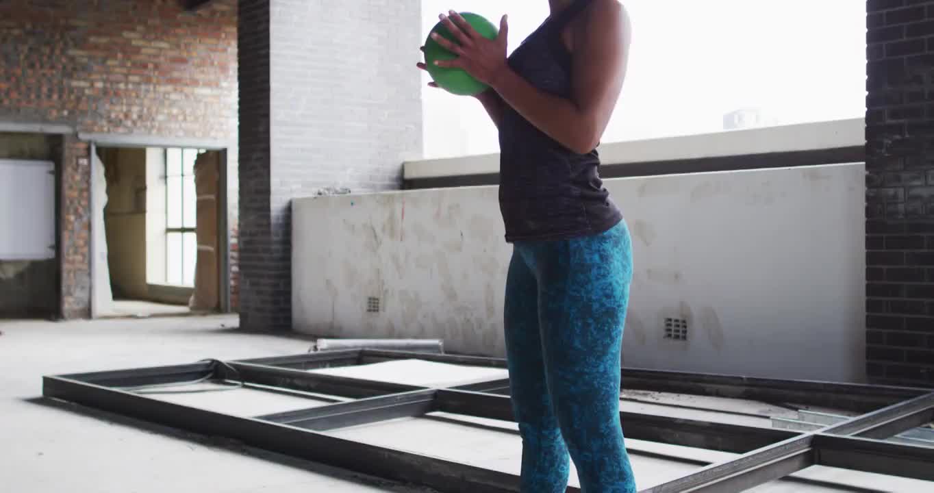 非裔美国妇女在一个空的城市建筑中练习实心球视频素材