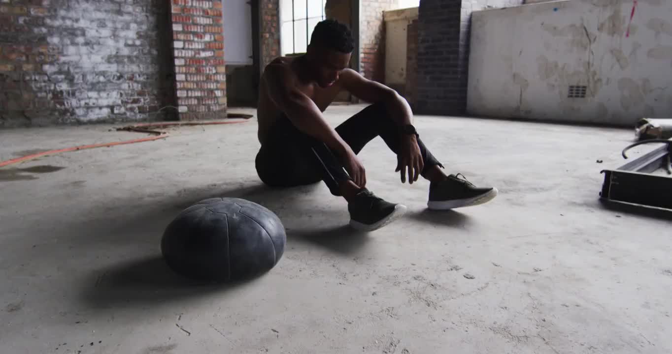 非裔美国人坐在休息后运动与实心球在一个空的城市建筑视频素材