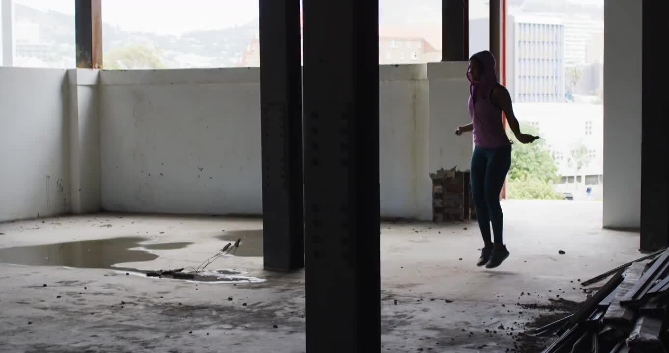 非裔美国妇女穿着连帽衫在空旷的城市建筑里跳绳视频素材