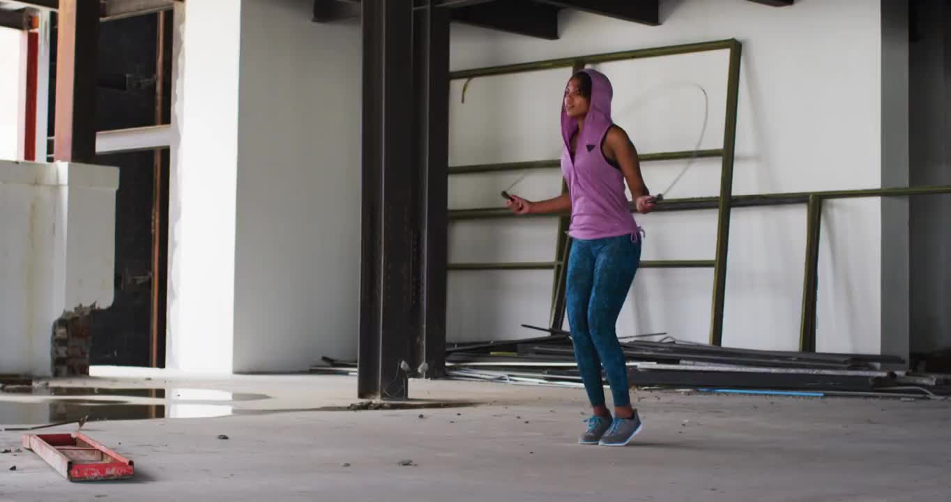 非裔美国妇女穿着连帽衫在空旷的城市建筑里跳绳视频素材