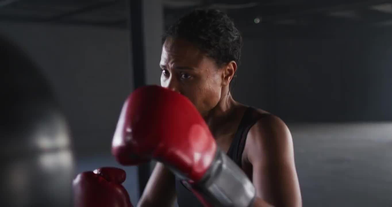 非洲裔美国妇女戴着拳击手套在空的建筑物训练出拳沙袋视频素材