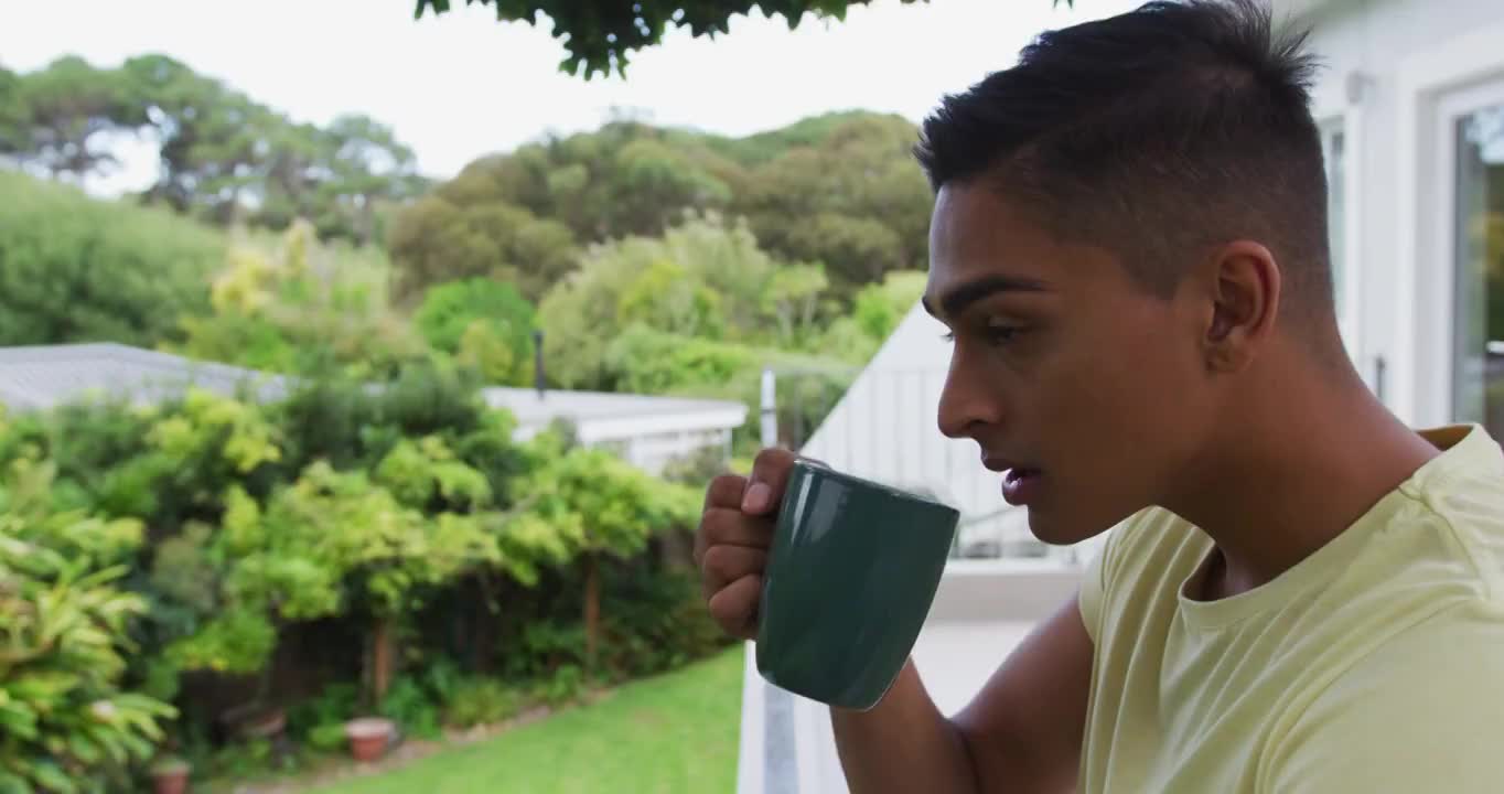 一个混血儿站在阳台上喝着一杯咖啡看着花园视频素材