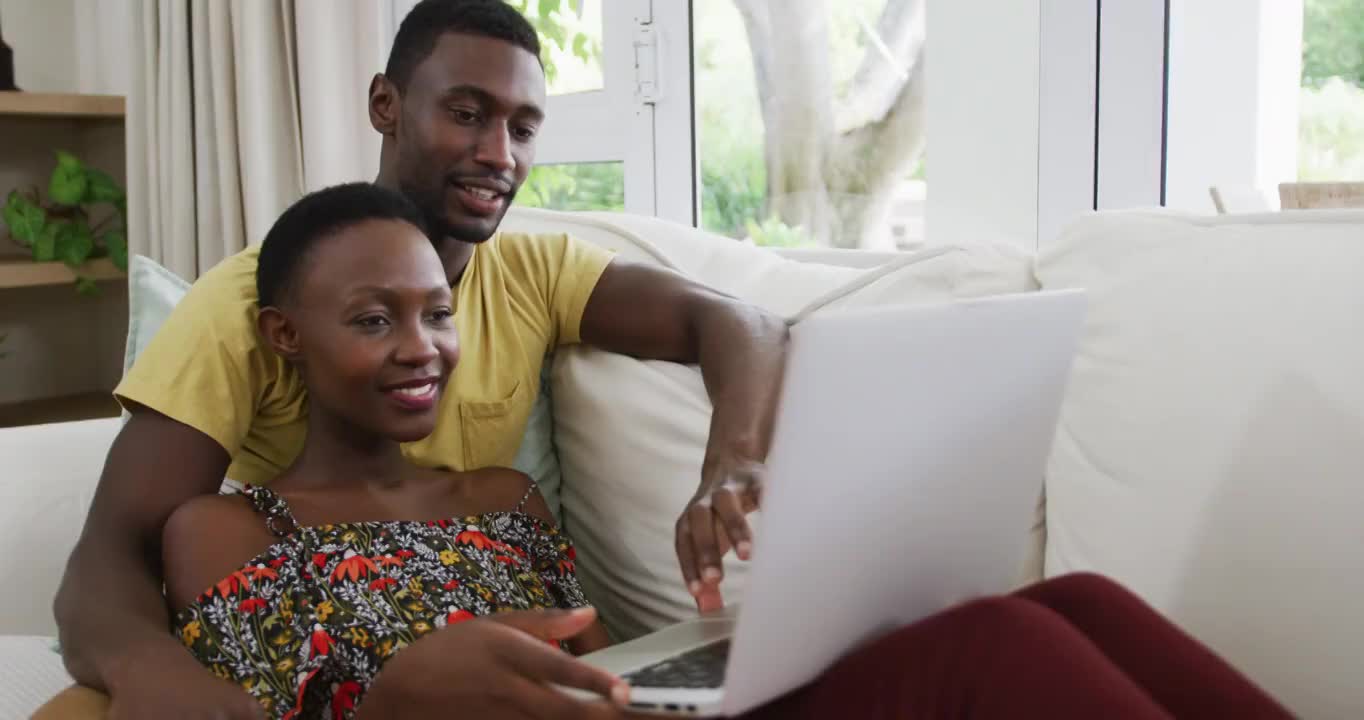 幸福的非裔美国人夫妇在沙发上拥抱和交谈看着笔记本电脑视频素材