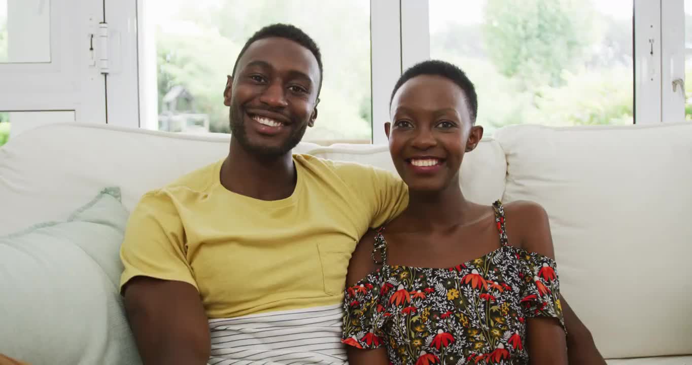 一对幸福的非裔美国夫妇坐在沙发上拥抱着镜头微笑视频素材