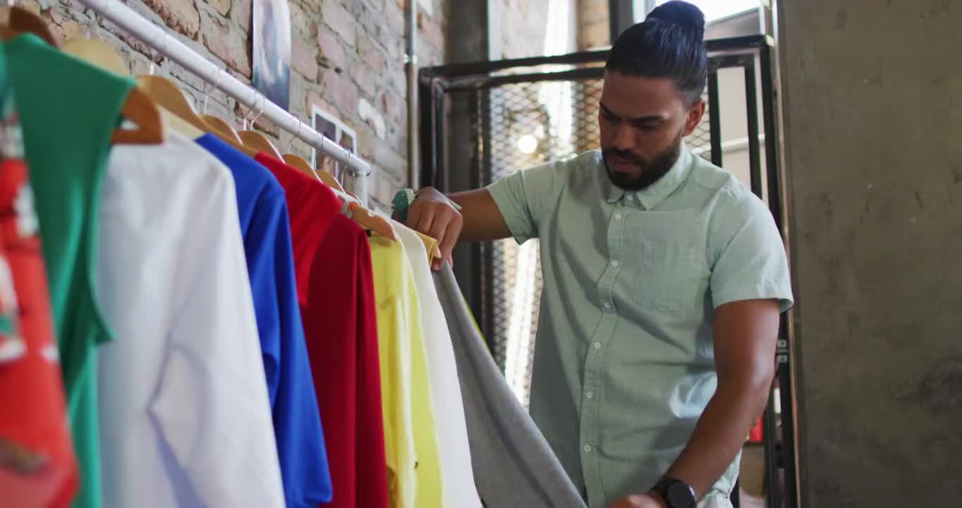 混血男性时装设计师看着不同的衣服和微笑视频素材