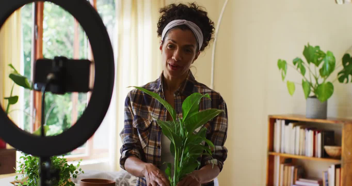 混血女视频博主在花盆里移植植物，并在家里用智能手机录制视频购买