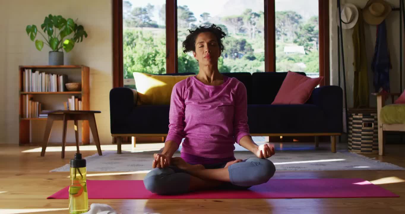 混合种族妇女练习瑜伽和冥想，而坐在瑜伽垫在家里视频下载