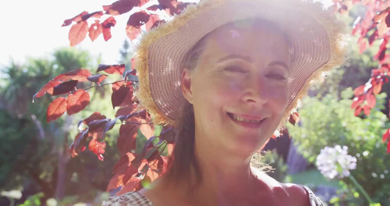肖像快乐的白人老年妇女在花园戴太阳帽和在阳光下微笑视频素材