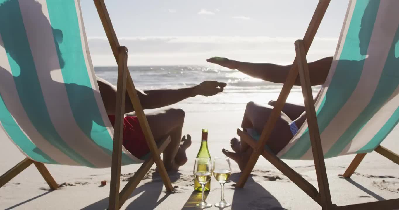 一对非洲裔美国夫妇手牵着手坐在海滩的躺椅上视频下载