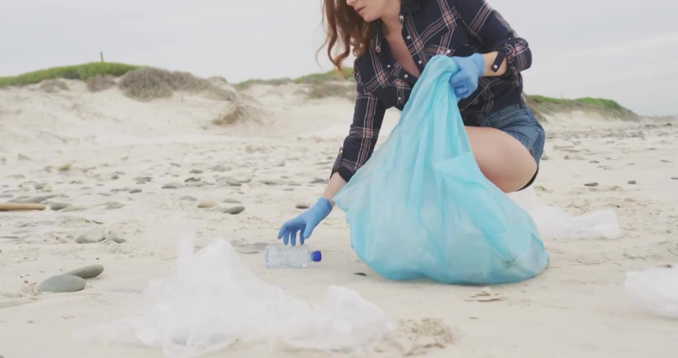 一个戴着乳胶手套的白人妇女在海滩上捡垃圾，望着前方视频素材