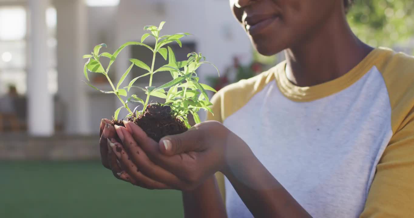 快乐的非洲裔美国女性园艺，持有和闻植物在花园里视频购买