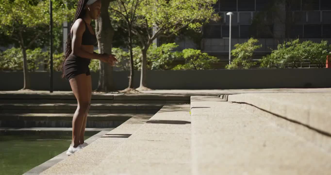 非裔美国妇女戴着无线耳机在户外运动，在城市里跳楼梯视频素材