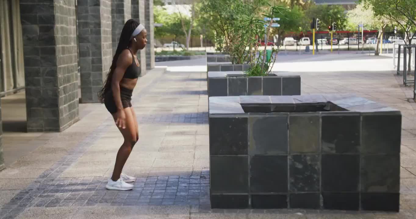 非裔美国妇女在户外运动，戴着无线耳机在城市里跳跃视频素材