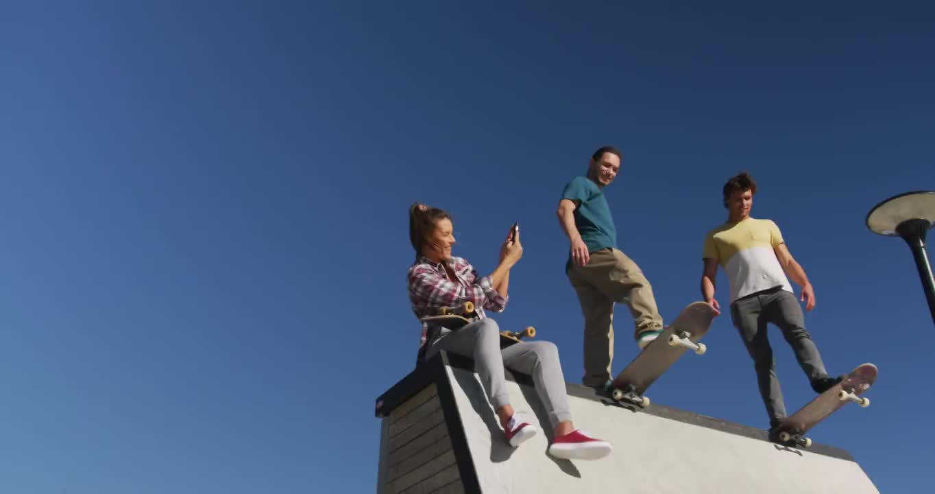 一个快乐的白人女人正在给她的两个男性朋友拍滑板照片视频下载
