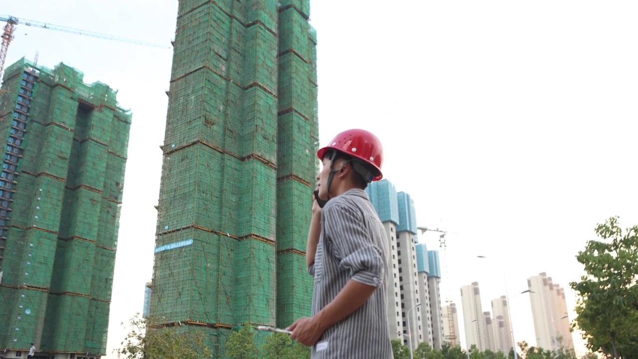 青年男性建筑工程师在未完工的大楼前打电话视频素材
