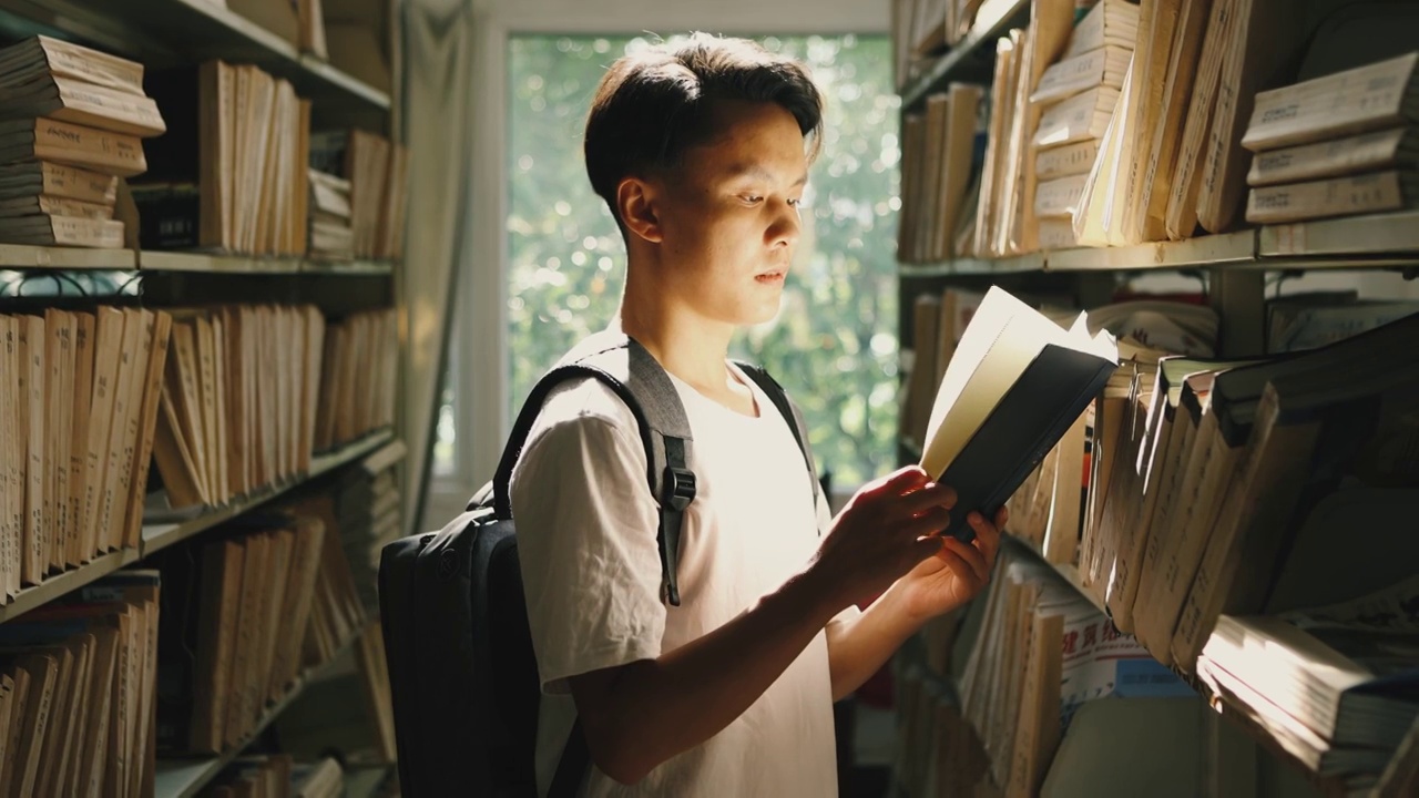 一个亚洲男性大学生在图书馆书架前阅读书籍视频素材
