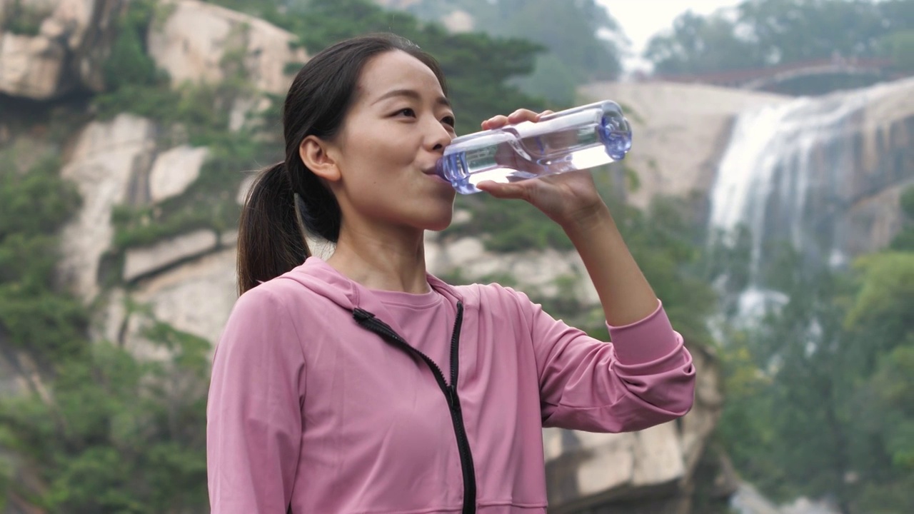 亚洲中国人女性在瀑布下喝水饮用水视频素材