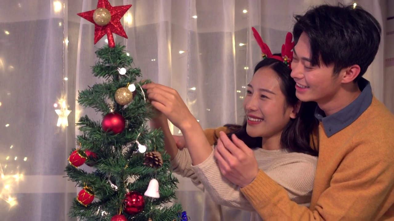 年轻情侣圣诞节在家装饰圣诞树视频素材