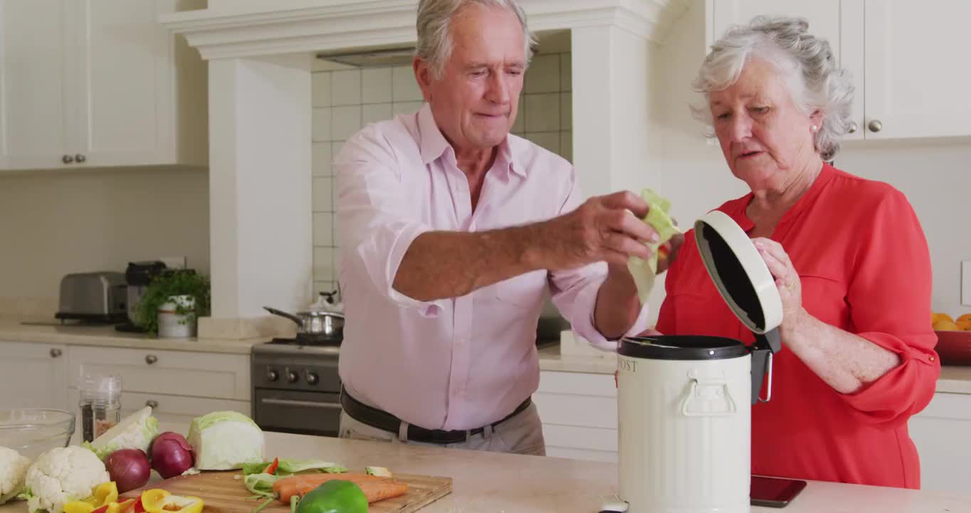 快乐的白人老年夫妇在厨房准备饭菜，堆肥蔬菜残渣视频下载