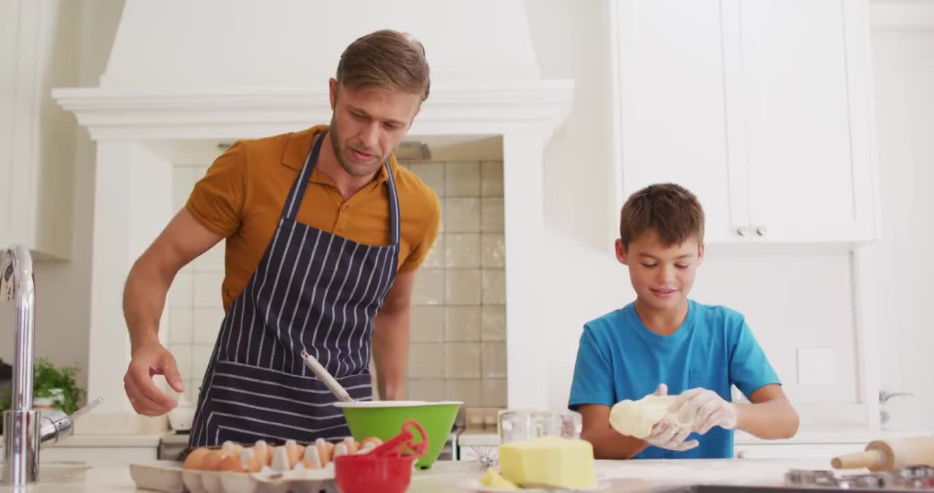 白种人的父亲和儿子在家里的厨房里一起使用数码平板电脑和烘焙视频素材
