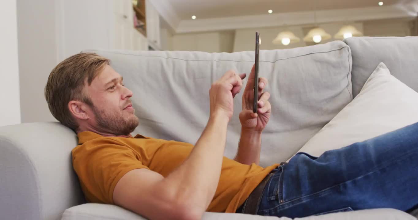 快乐的白人男人躺在沙发上用平板电脑的肖像视频素材