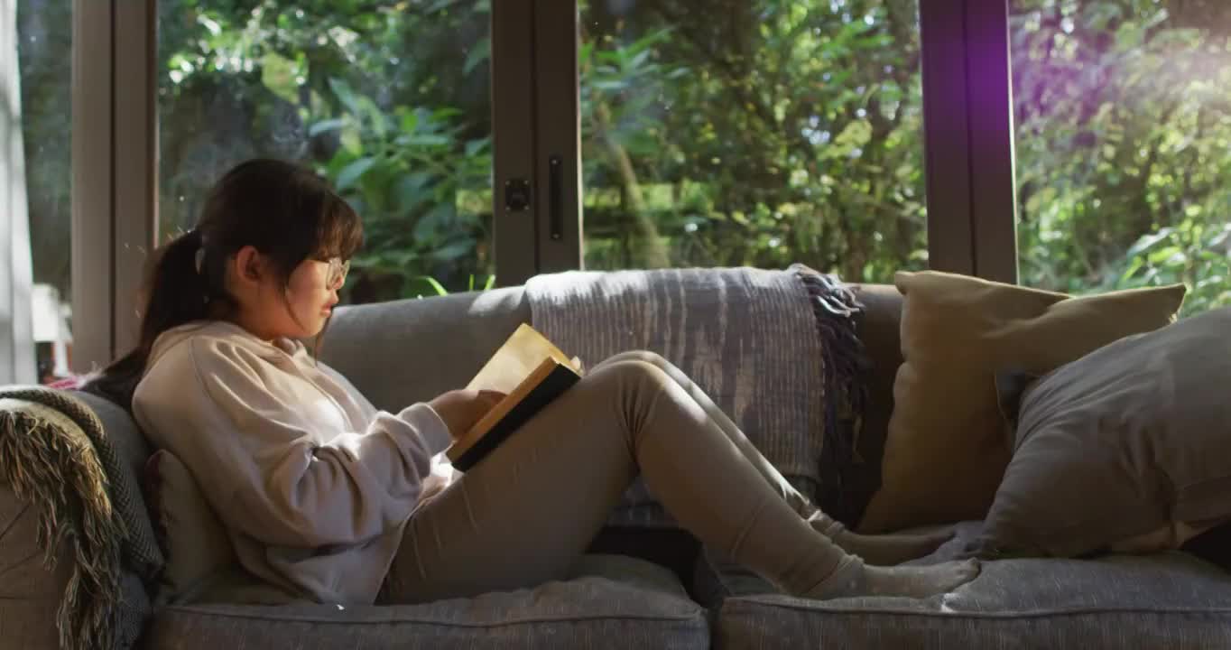 亚洲女孩微笑着坐在家里的沙发上看书视频下载