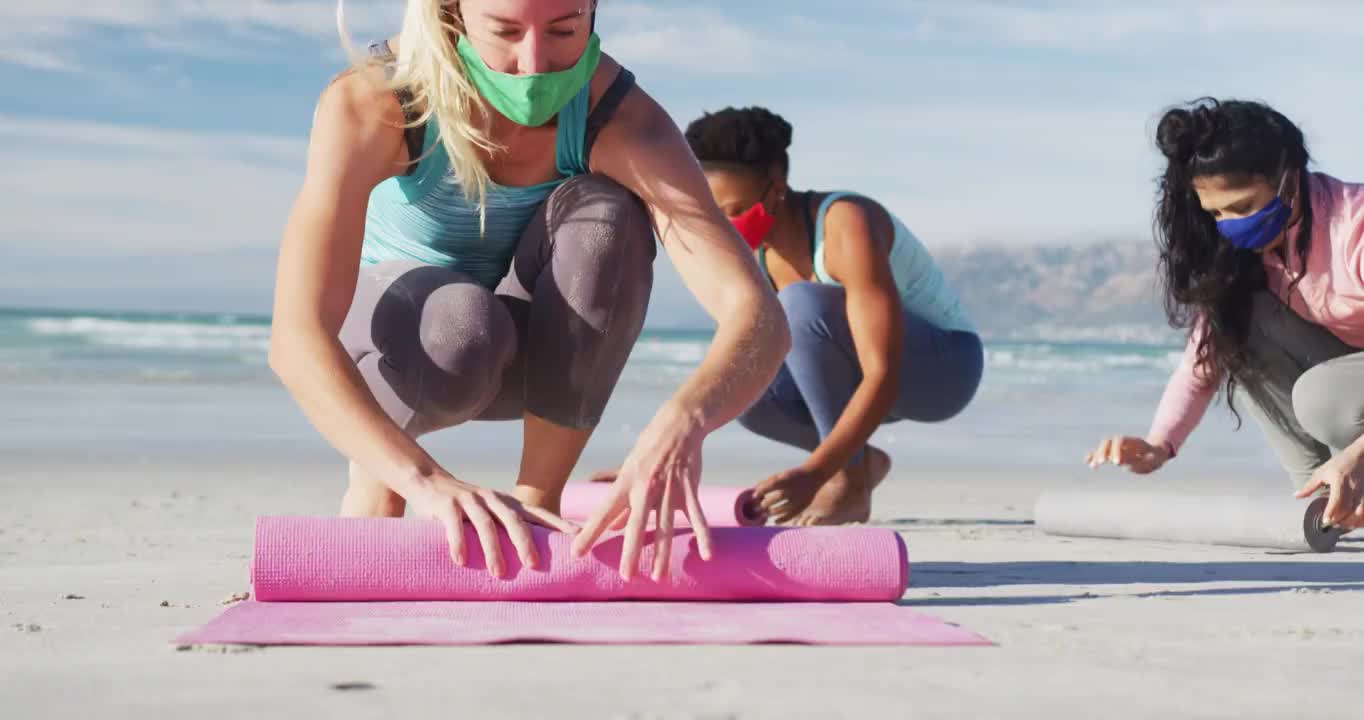 一群不同的女性朋友戴着口罩在海滩上滚动瑜伽垫视频下载