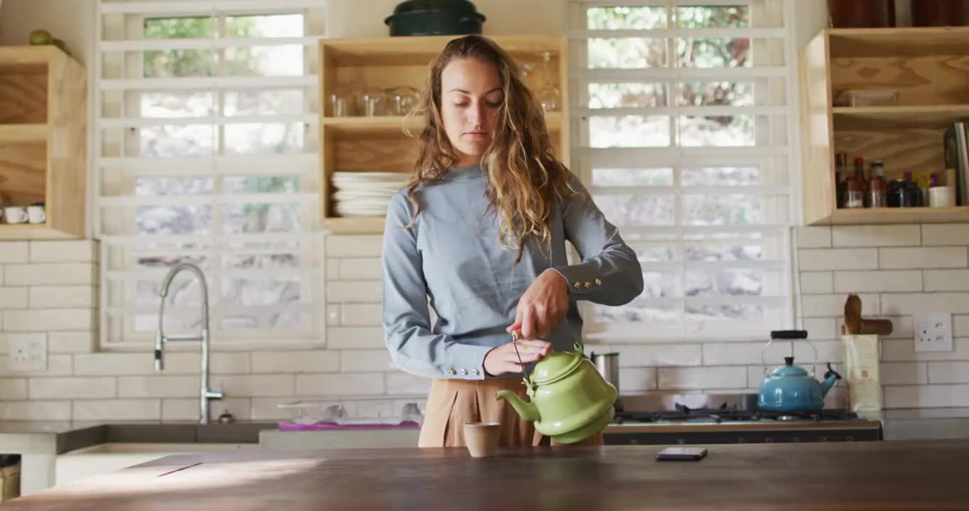 快乐的白人妇女站在柜台在村舍厨房倒从壶和微笑视频下载