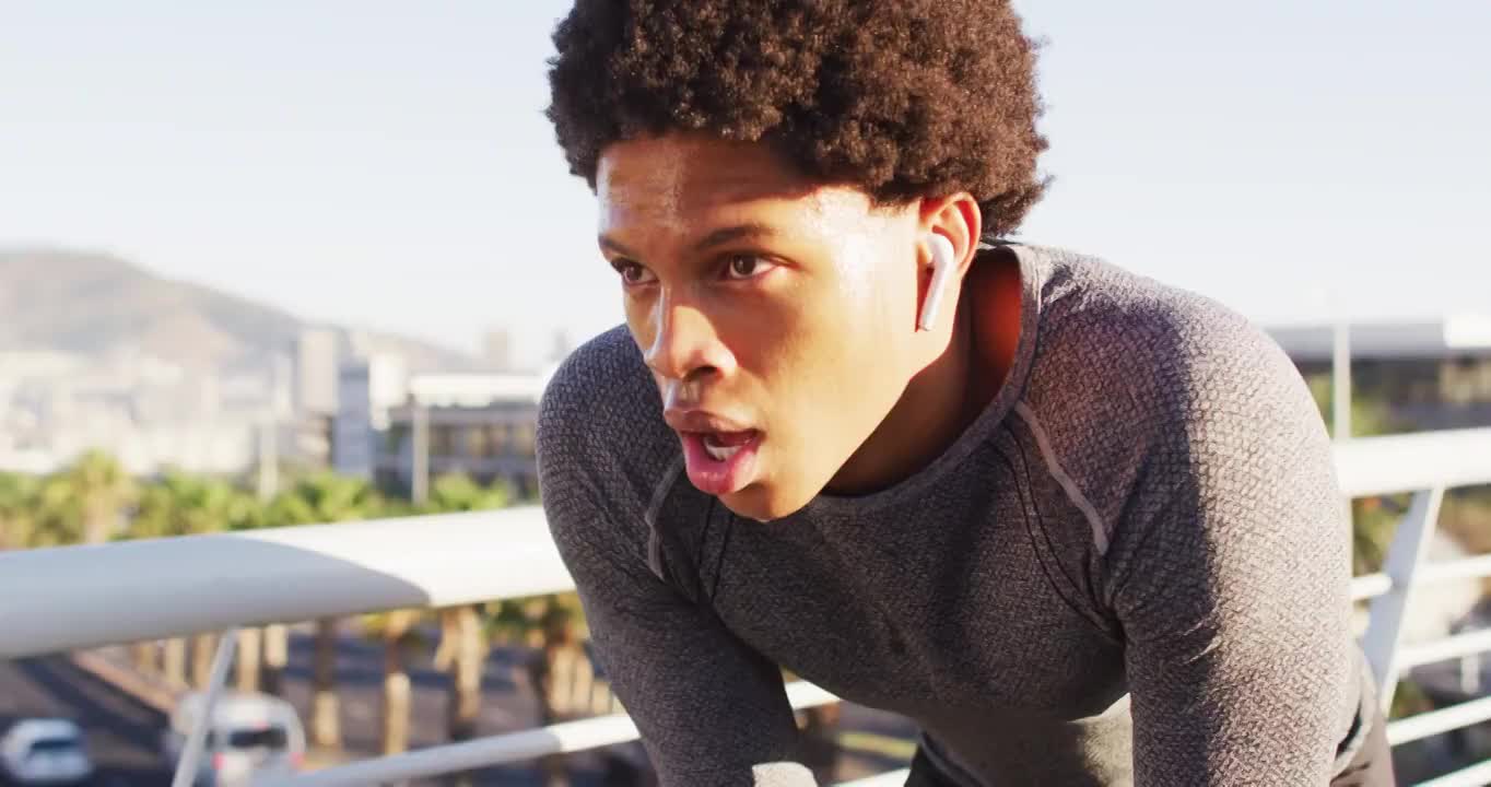 健康的非裔美国人在城市户外运动，戴着无线耳机，在人行天桥上休息视频购买
