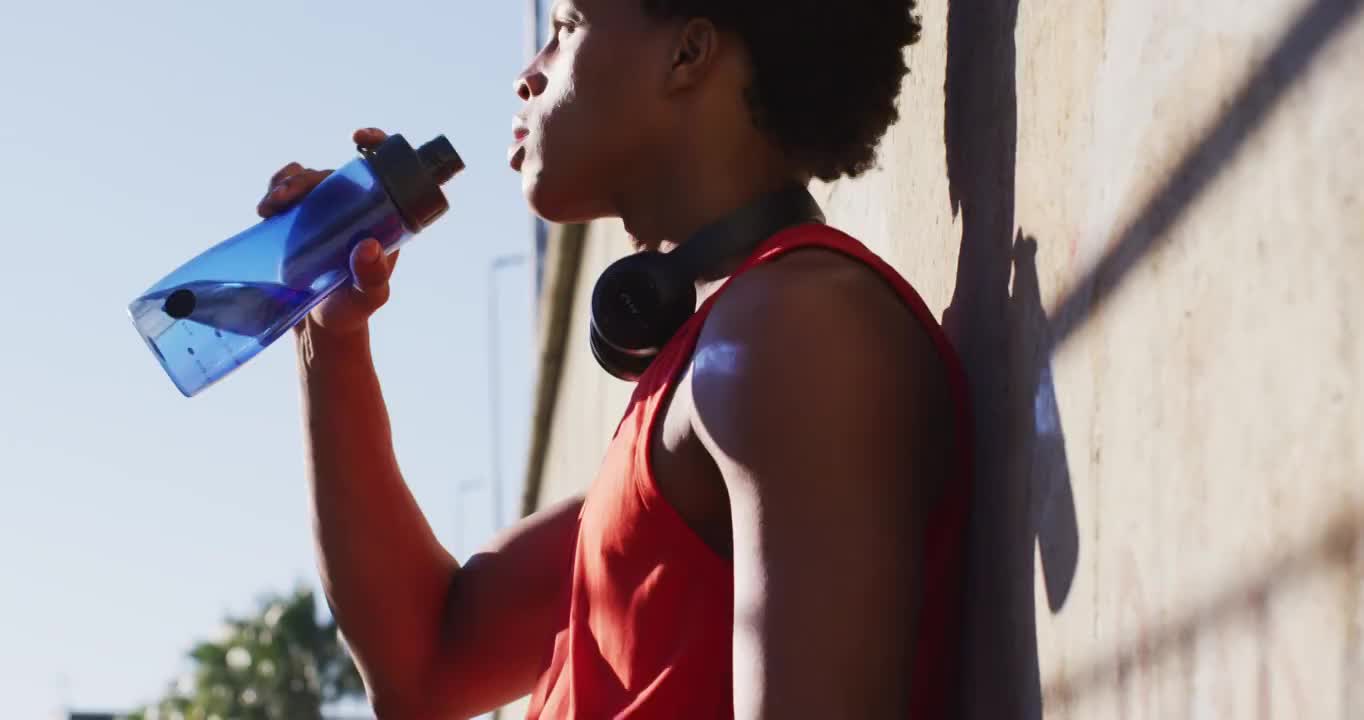 健康的非洲裔美国人在城市锻炼休息，靠在墙上喝水视频素材