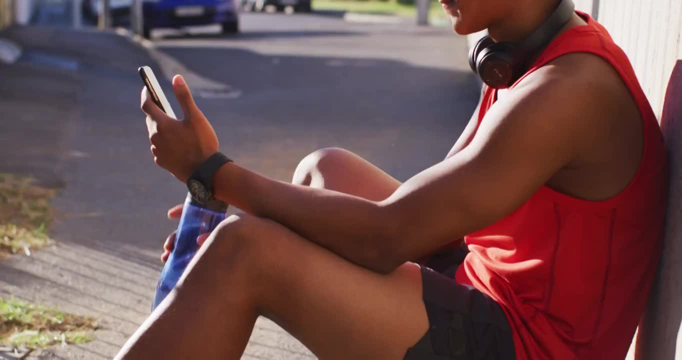 健康的非洲裔美国人在城市锻炼休息，使用智能手机，坐着喝水视频素材