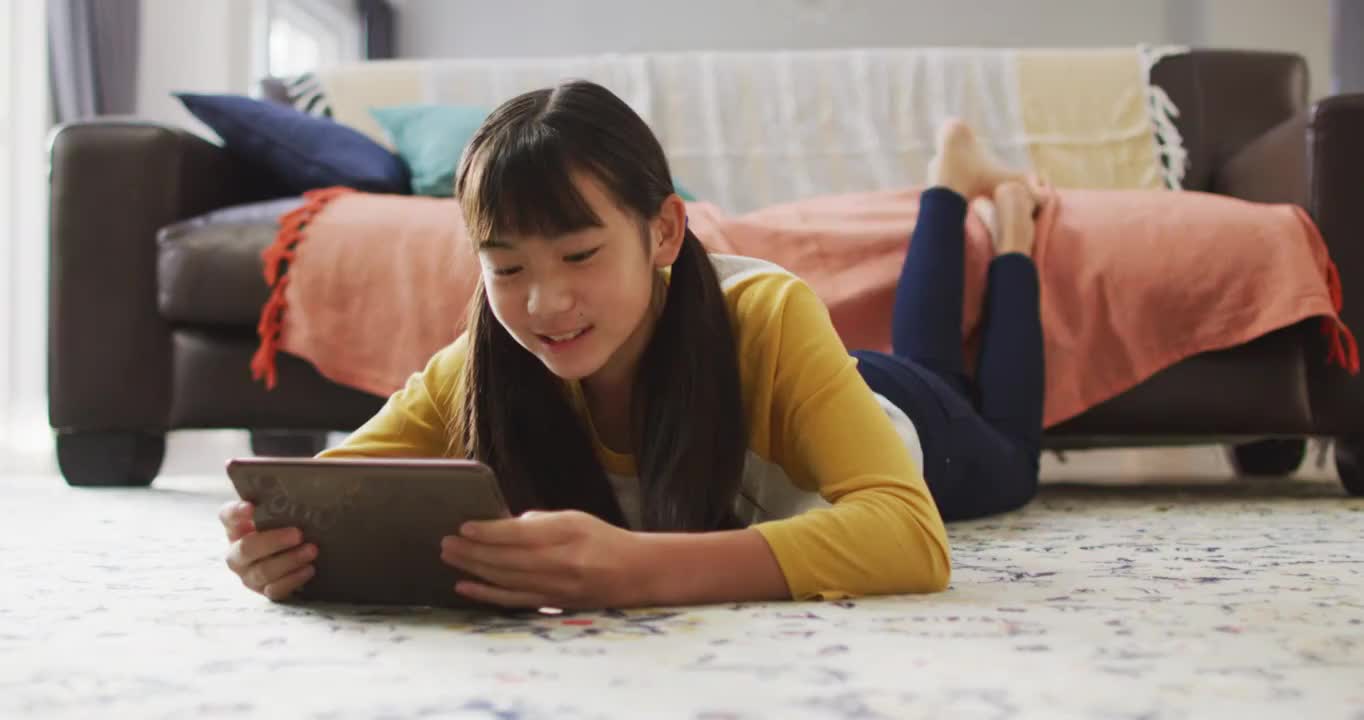 亚洲女孩微笑和使用平板电脑躺在家里的地板上视频下载