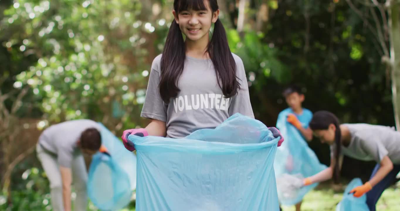 微笑的亚洲女孩穿着志愿者t恤，拿着垃圾袋收集塑料垃圾视频下载
