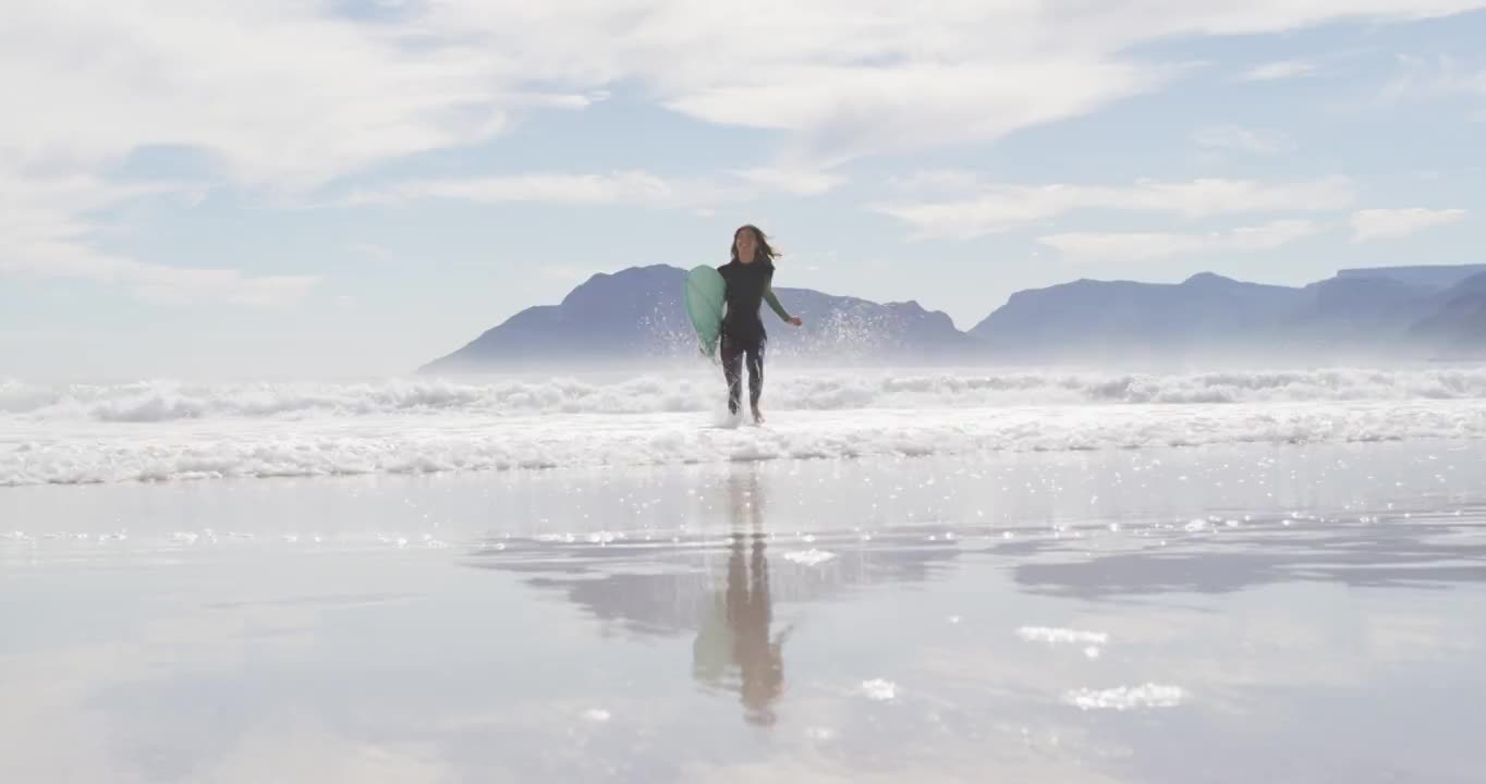 一个混血儿女人带着冲浪板从海边跑到海滩上视频素材