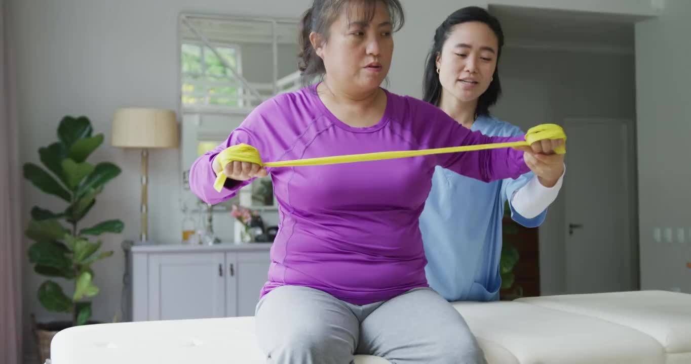 亚洲女性理疗师帮助女性患者在手术中用运动带锻炼手臂视频素材
