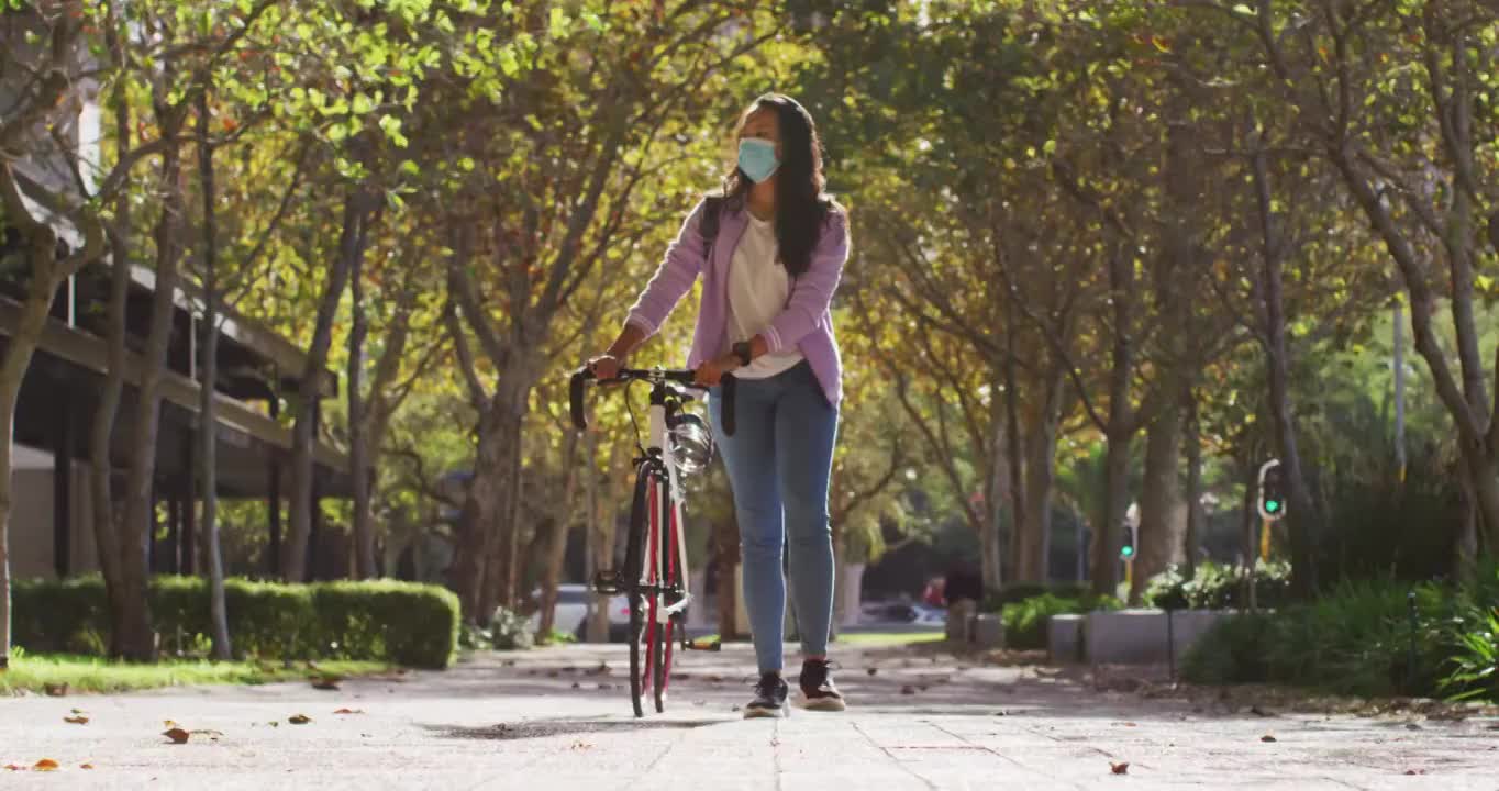 亚洲妇女戴着口罩和自行车在公园里散步视频素材
