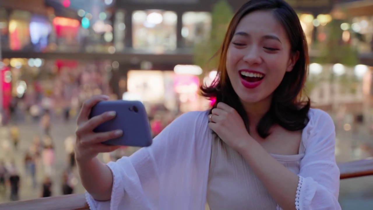 美丽的亚洲年轻女子晚上在城市街道上使用手机视频素材