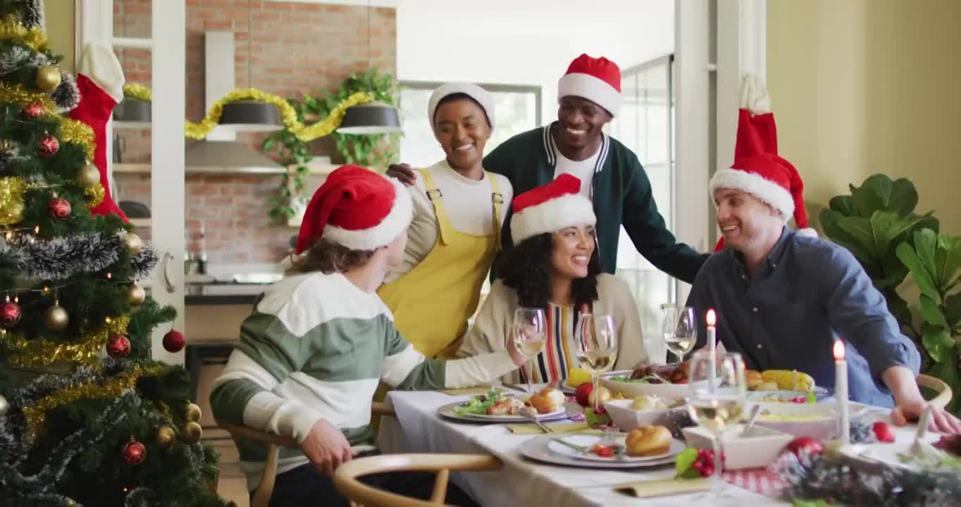 快乐的一群不同的朋友，戴着圣诞帽庆祝大餐，在圣诞节期间拍照视频下载