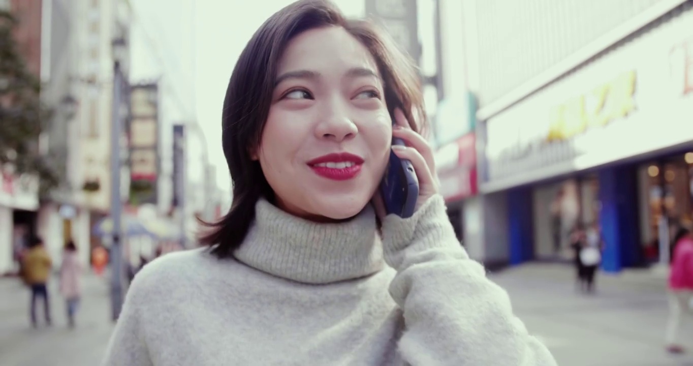 一个女孩正在步行街上愉快地用手机和别人交谈。视频素材