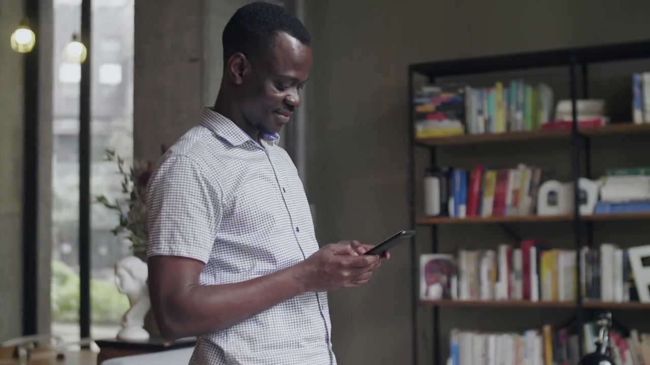 一位非洲黑人商人站在窗前喝咖啡，用手机交谈的侧视图视频素材