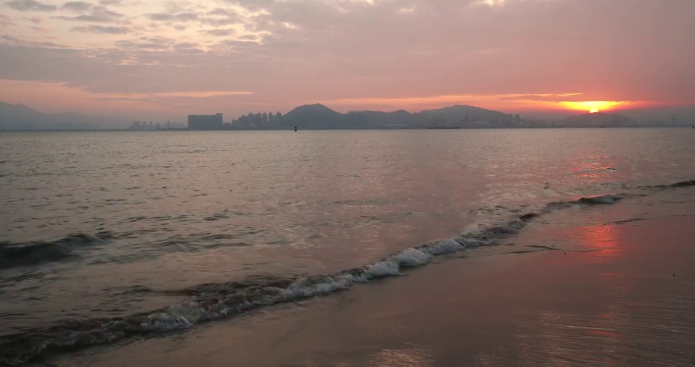 在中国福建厦门的晨光中，海岸的波浪拍打着海滩，太阳从山后升起视频素材