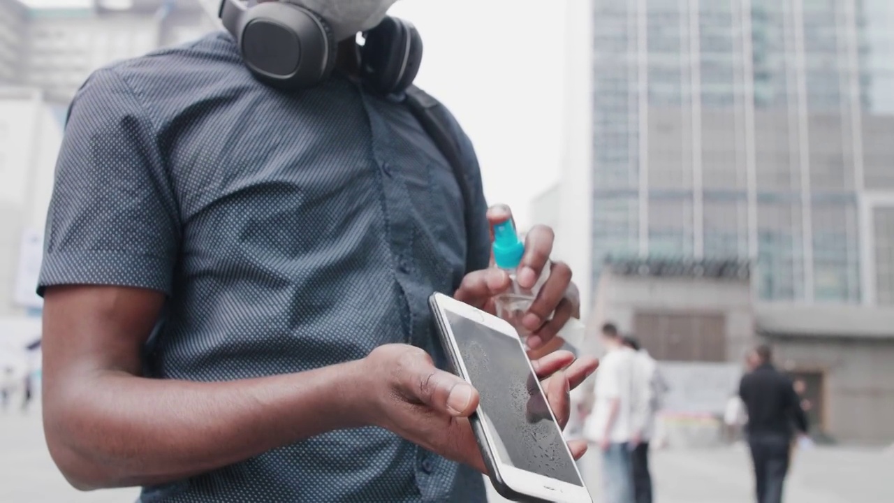 一个黑人男生戴着口罩在城市的街道上看手机视频素材