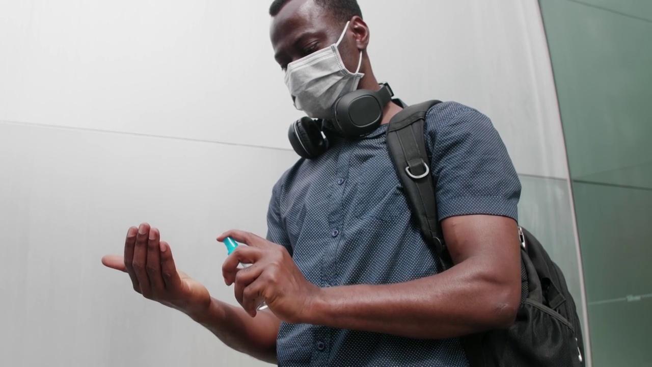 一个黑人用消毒喷雾喷手戴着口罩走在街上视频下载
