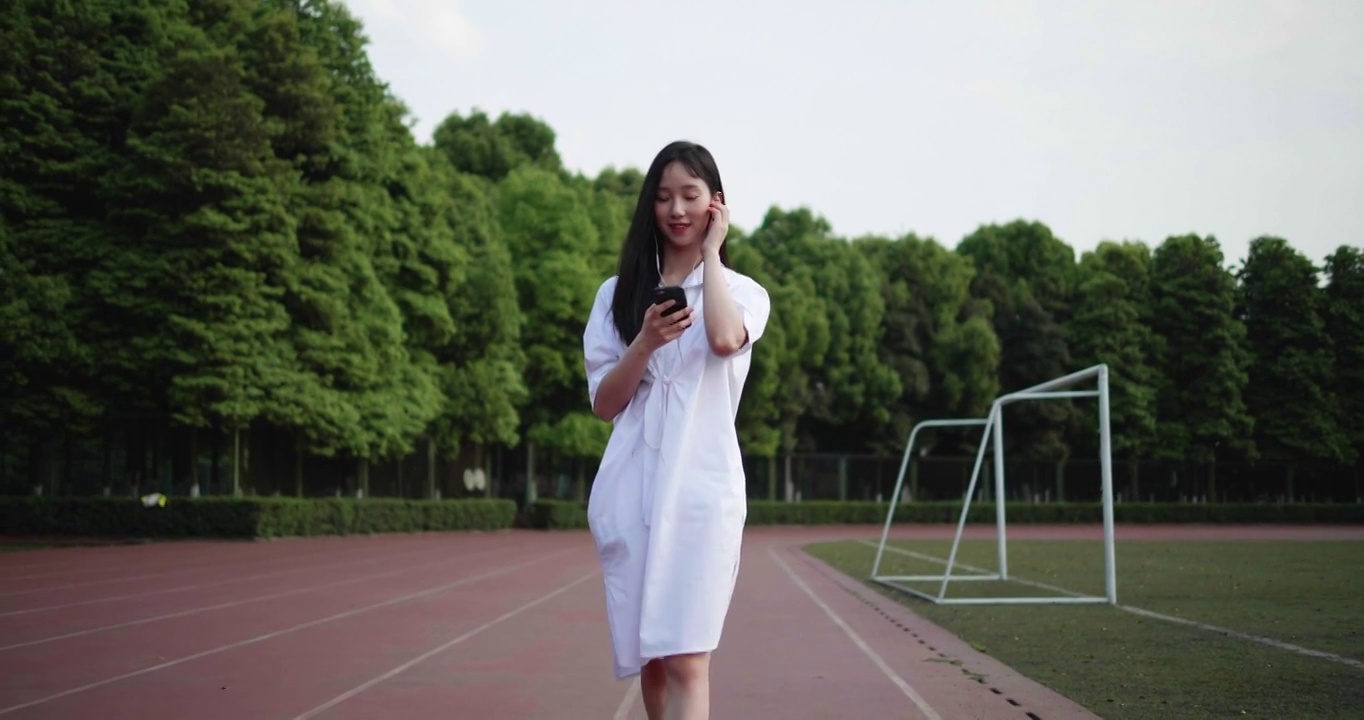 一个漂亮的中国女孩在操场上听音乐视频素材