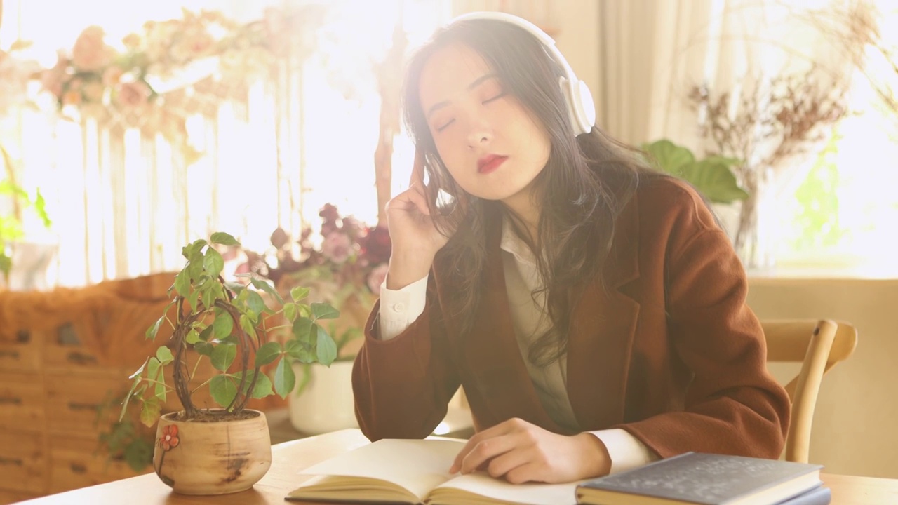 一个亚洲美女在室内带着耳机休息看书放松视频素材
