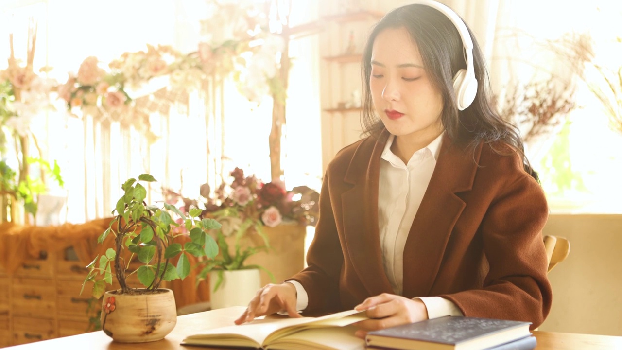 一个亚洲美女在室内带着耳机休息看书放松视频素材
