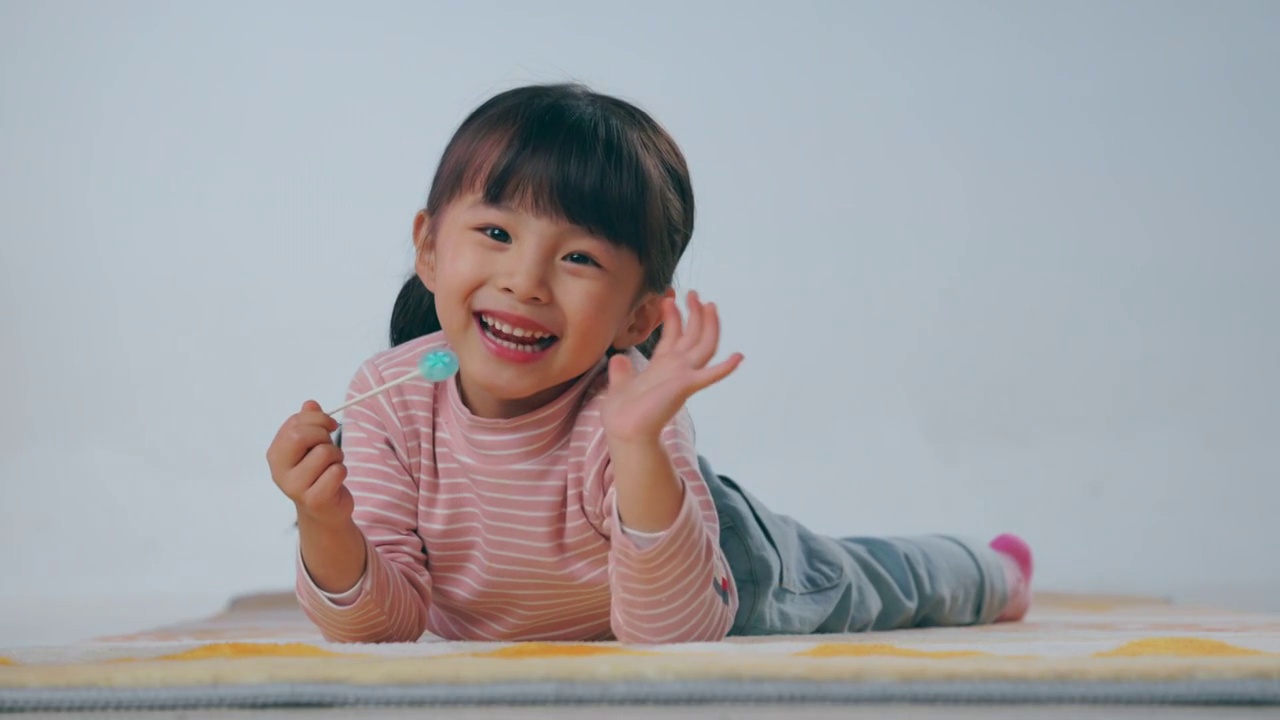 快乐的小女孩趴在地毯上吃棒棒糖视频下载