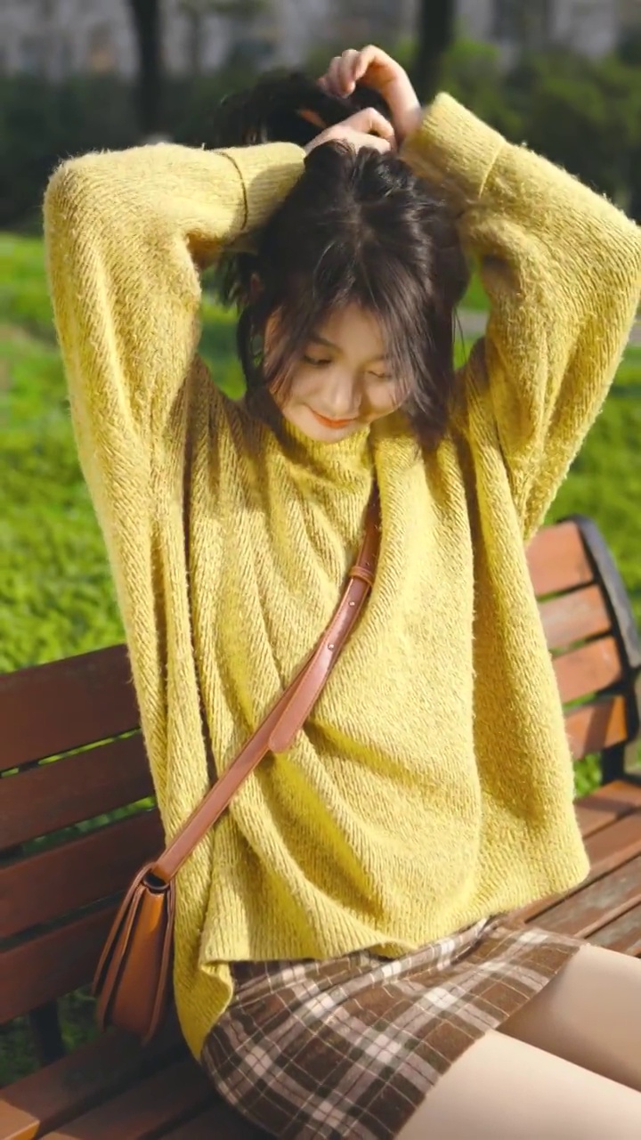 一个青年女性坐在公园的椅子上扎头发视频素材