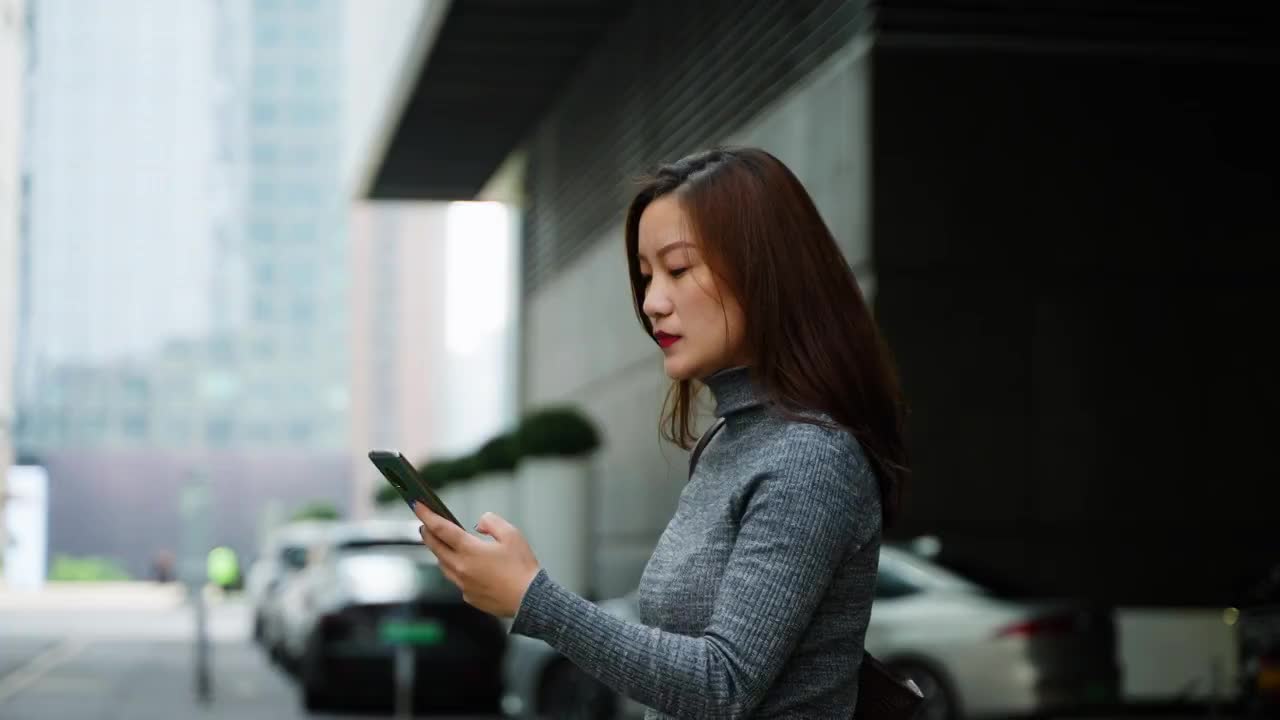 一位年轻女人拿着手机发消息走在城市街道视频下载