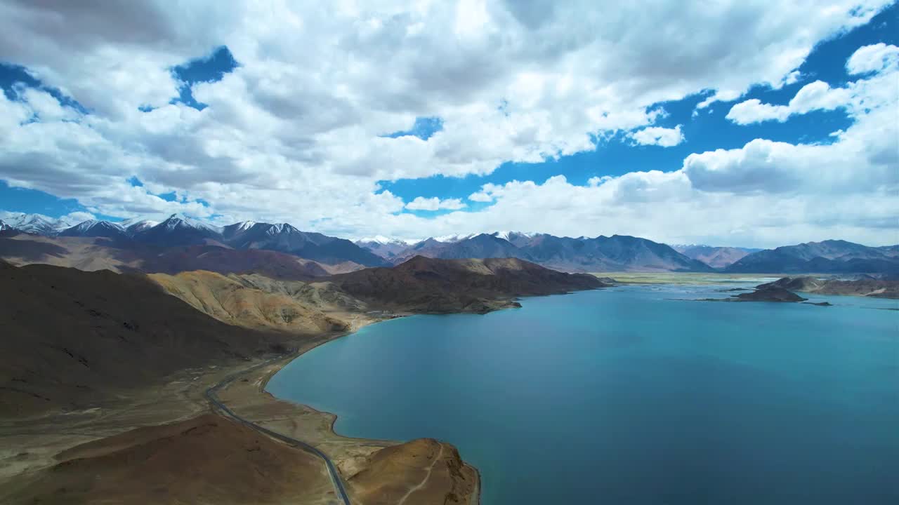 西藏阿里班公湖，六月晴朗的天气，航拍蓝天白云下，湖水湛蓝，雪山环抱，新藏公路从湖边经过。视频下载